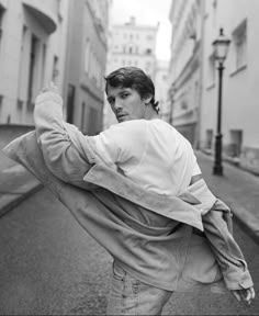 black and white photograph of a young man in the middle of an alleyway holding his jacket over his shoulders