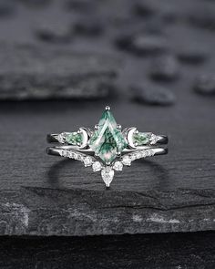 an engagement ring with green and white diamonds on top of a black stone slabd surface