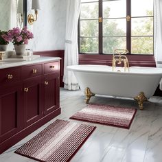 a bathtub and rugs in a bathroom with red cabinetry, windows, and white marble countertops