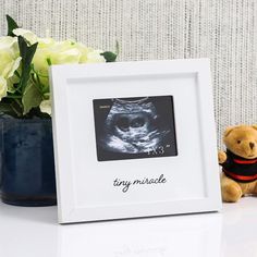 a teddy bear sitting next to a white frame with a baby's photo on it