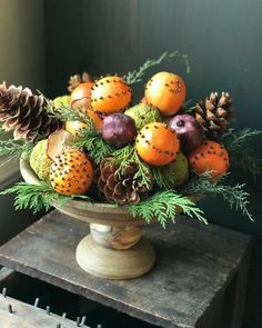 a vase filled with lots of different types of fruit and pine cones on top of a wooden table