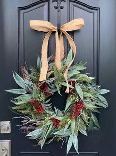 a wreath on the front door of a house decorated with greenery and pine cones