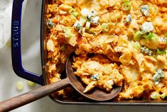 a casserole dish with chicken, cheese and green onions in it next to a wooden spoon