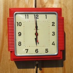 a red and white clock sitting on top of a wooden wall