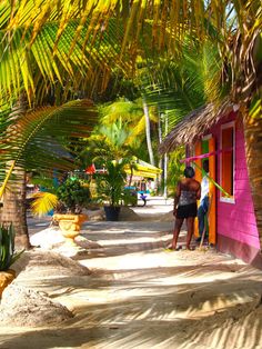 two people standing in front of a pink building with palm trees on the side walk