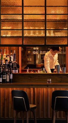 a man is behind the bar at a restaurant with many bottles on the counter and two stools in front of him