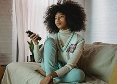 a woman sitting on a couch holding a remote control