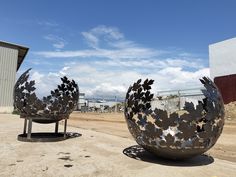 two large metal sculptures sitting on top of a dirt field next to a building and blue sky