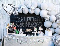 a table topped with white balloons next to a chalkboard sign that reads, the infinitity and beyond