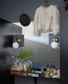 a mirror that has some lights on it and a coat hanging from the wall above it