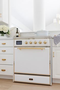 a white stove top oven sitting inside of a kitchen next to wooden floors and cabinets