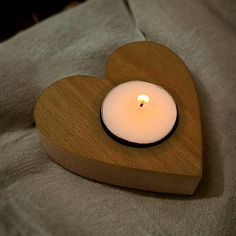 a wooden heart shaped candle holder with a lit candle in the middle on a bed