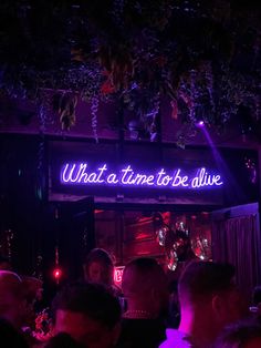 a group of people standing in front of a neon sign that reads what a time to be alive