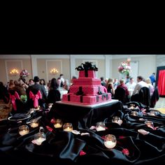 a large red cake sitting on top of a table covered in black cloth and candles