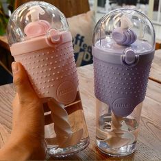 two baby bottles sitting on top of a wooden table next to each other, one with a pacifier in it