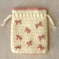 a crocheted bag with pink bows on it sitting on a white carpeted floor