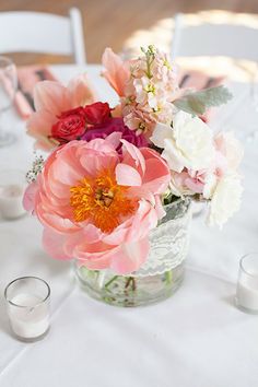 a vase filled with pink and white flowers on top of a table next to candles