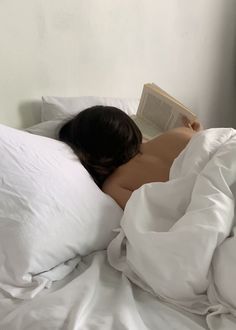 a woman is laying in bed with her head on the pillow and reading a book