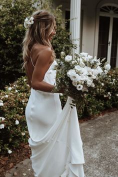 a woman in a white dress holding a bouquet of flowers and walking down the street