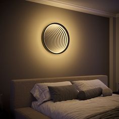 a bed with pillows and blankets under a round light fixture on the wall above it