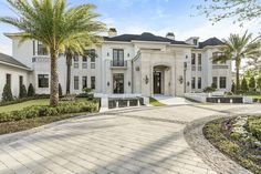 a large white house with palm trees in the front yard and landscaping on either side