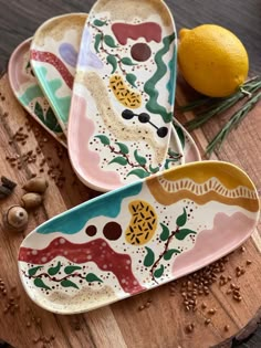 two colorful plates sitting on top of a wooden cutting board next to an orange and some spices