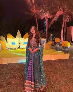 a woman standing in front of a palm tree wearing a blue and pink dress with an intricate