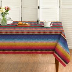 a table covered with a multicolored tablecloth next to a vase filled with flowers