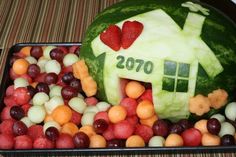 a watermelon shaped like a house surrounded by grapes and strawberries in a tray