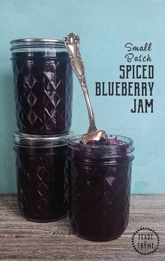 three jars filled with blueberry jam on top of a wooden table next to a spoon