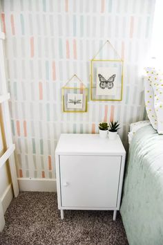 a small white dresser next to a bed in a room with striped wall paper on the walls