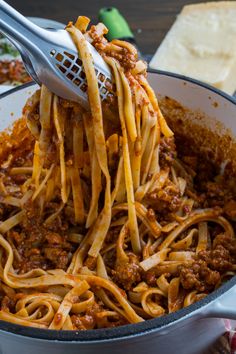 spaghetti being cooked in a skillet with a ladle full of sauce and cheese