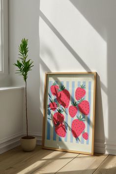 a painting with strawberries is on the floor next to a potted plant and window