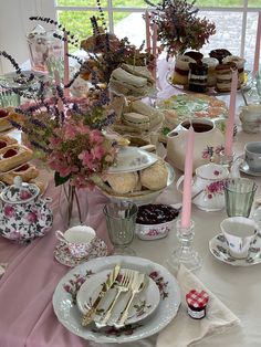 the table is set with tea cups, plates and desserts