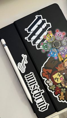 a black notebook with stickers on it and a white pen next to the cover