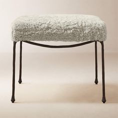 an upholstered bench with metal legs and a white sheepskin seat cover on it