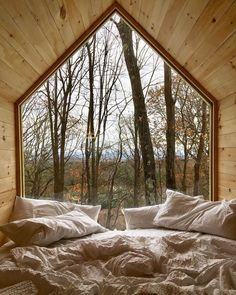 a bed with white sheets and pillows in front of a window that looks out onto the woods