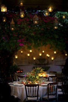 an outdoor dining area with tables, chairs and hanging flowers on the wall behind them