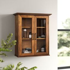 a wooden cabinet with glass doors on the wall next to a potted plant and window