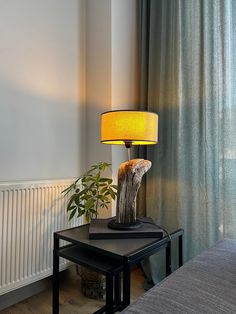 a table with a lamp on top of it next to a bed and a window