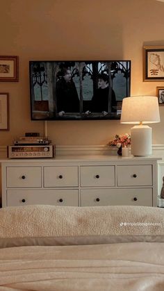 a bedroom with a bed, dresser and television mounted on the wall over it's headboard