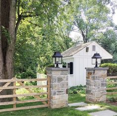 a white shed with two lamps on top of it next to a fence and trees