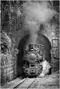 black and white photograph of an old train coming out of a tunnel