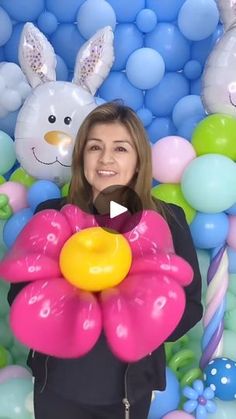 a woman holding a large balloon flower in front of balloons and bunnies with bunny ears on them