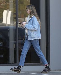 a woman walking down the street with her cell phone in her hand and she is wearing a denim jacket