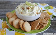 a bowl of whipped cream surrounded by crackers and limes on a green plate