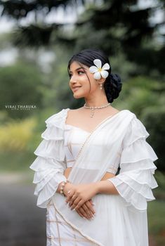 a woman wearing a white dress and flower in her hair, standing on the street