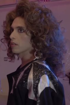 a man with long curly hair standing in front of a mirror wearing a black and white shirt