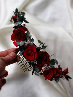 a person holding a comb with red roses on it and greenery around the comb