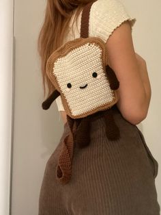 a woman is holding a crocheted bag with a smiling face on it's back